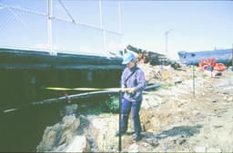 A scientist walking on the empty ground beside the harbour, the submarine is in the background.
