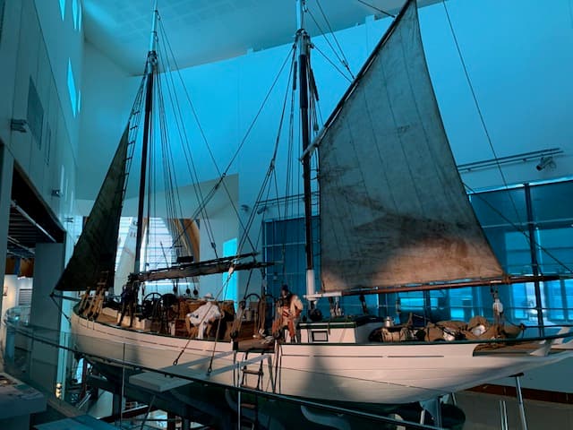 A pearling lugger on display in a gallery with sails hoisted. Figurines are on board representing a Master Pearler and a diver.