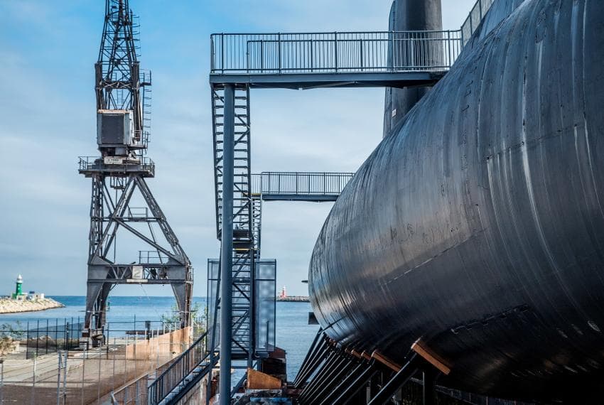 Looking down the long steel side of the submarine, we can see one of the old Harbour loading towers, and the harbour opening to the sea.
