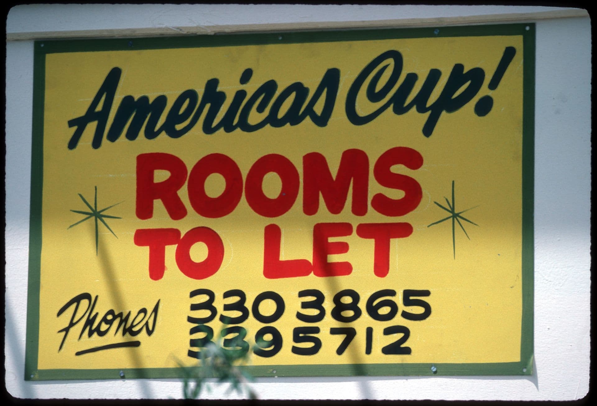 A sign reading "America's Cup! Rooms to let," followed" by two phone numbers with area codes 330 and 339.