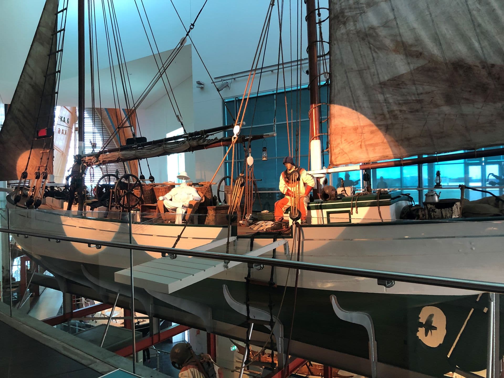 A large white and dark green sailing boat suspended next to the top floor. A mannequins in a diving suit sits  on the deck.