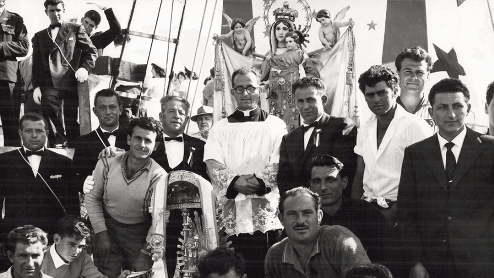 A Catholic priest and statue of Mary surrounded by parade participants.