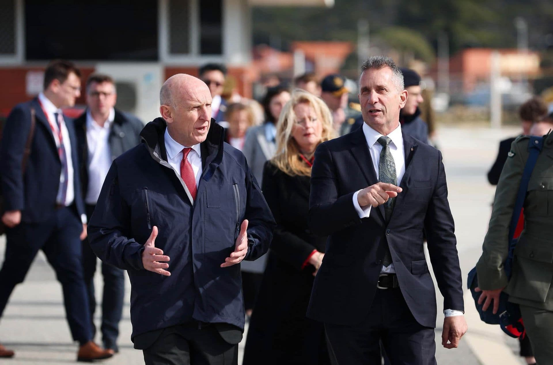 Two men wearing suits in an important discussion as they walk a busy street.