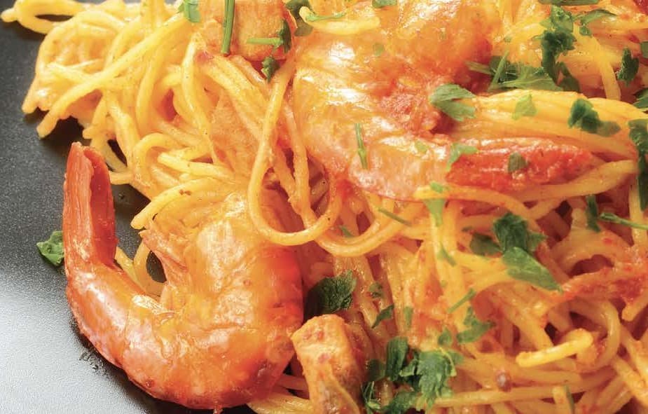 Vibrant orange prawns sit atop long strands of spaghetti garnished with parsley, on a black plate