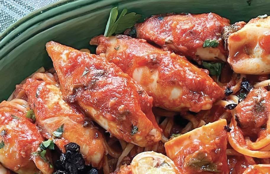 squid in a tomato sauce lie nestled on a bed of spaghetti in a green bowl.