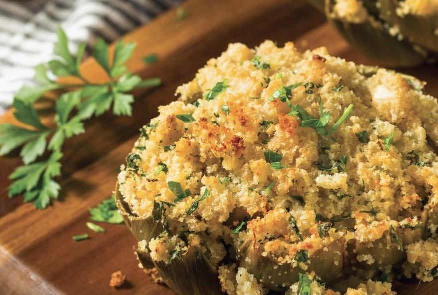 A browned crumbed artichoke on a wooden board garnished with parsley