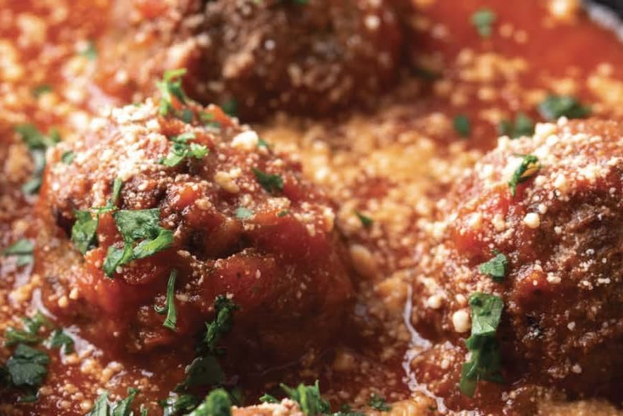 Browned cooked meatballs in a red tomato sauce and topped with finely grated cheese and parsley