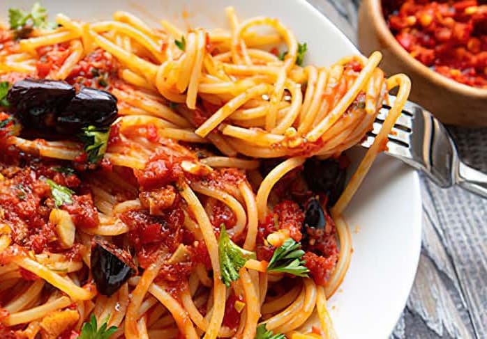 Strands of spaghetti twirled around a fork in red sauce, in a white shallow bowl.