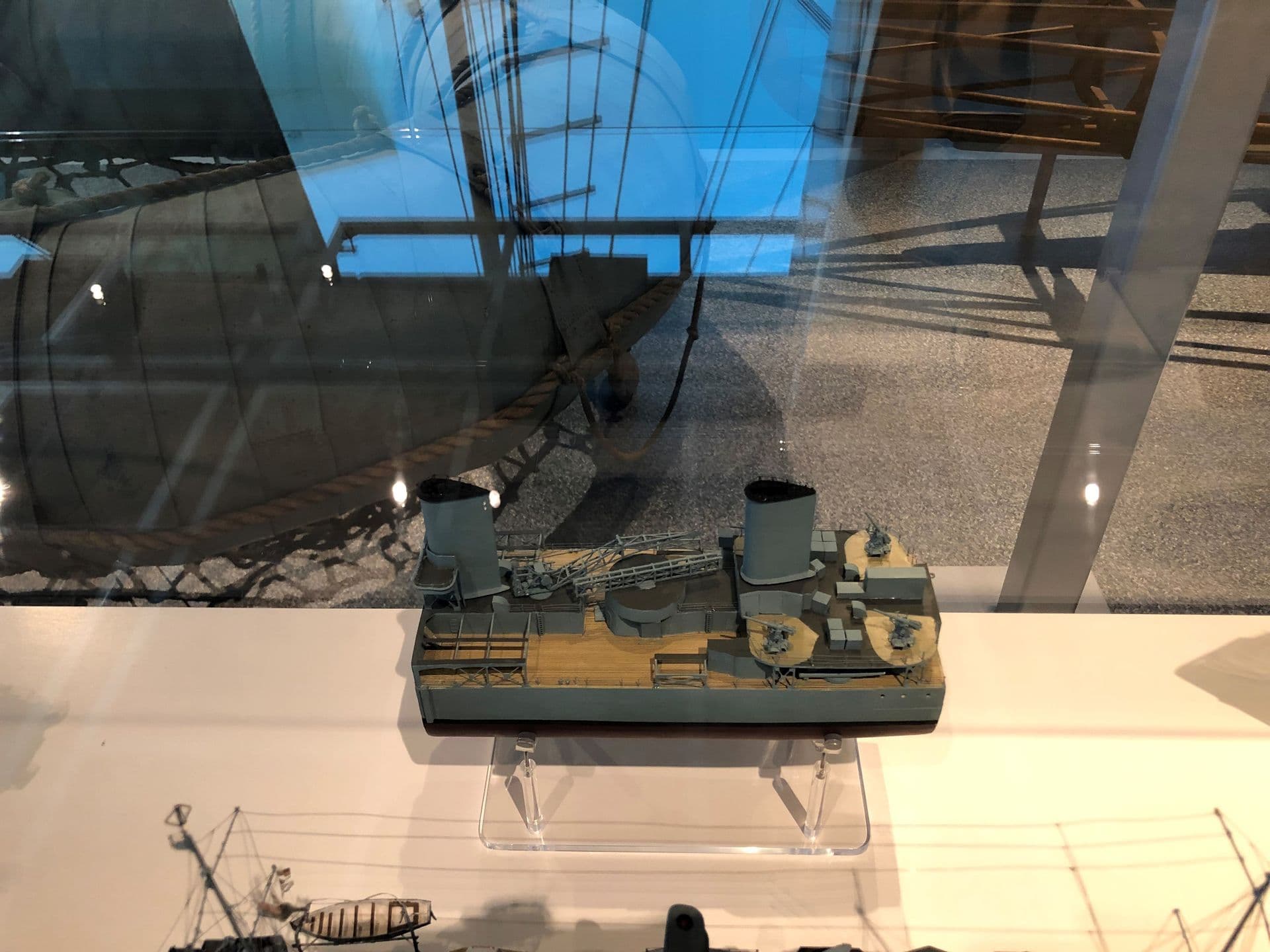 In a display case is a small section of a ship model. The model ship is painted grey, the section has two funnels and a wooden deck.